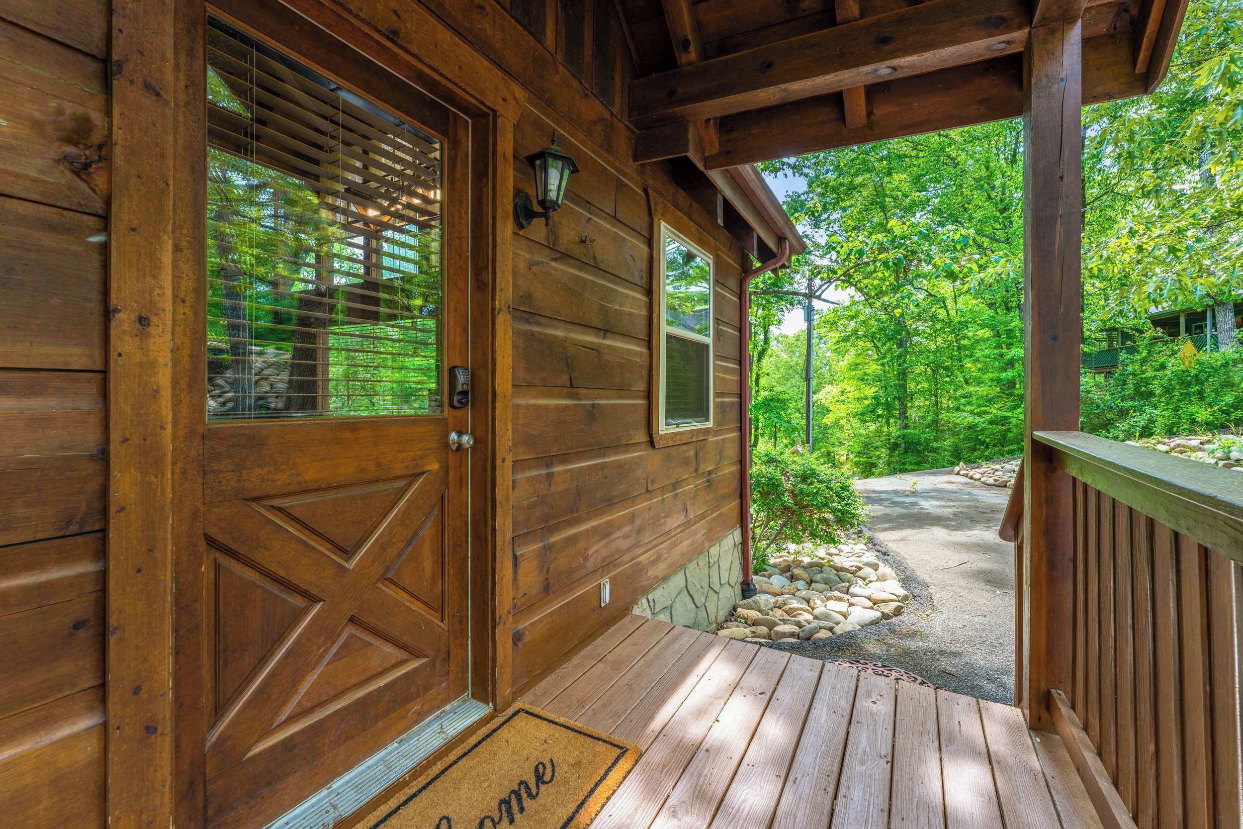 A wooden cabin with a porch, a door with a window, and a welcome mat.