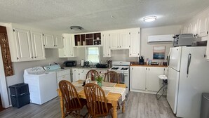 A kitchen with white cabinets, a dining table with chairs, a washing machine, and a refrigerator. - Beautiful 2-bedroom cottage with AC in charming Lanexa (Lanexa)