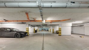 A parking garage with a car parked on the left, concrete floors, and pillars with yellow and black stripes. - Valor by Grand Apartments (Sopot)