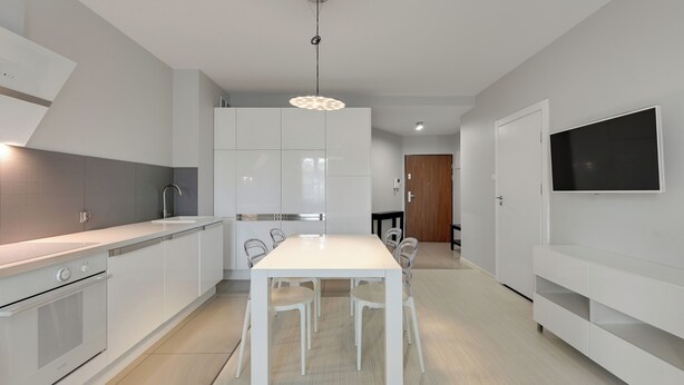 A modern kitchen with white cabinetry, a dining table, and chairs. - Valor by Grand Apartments (Sopot)