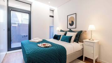 Quarto com cama, mesa de cabeceira, luminária, quadro emoldurado e porta deslizante.