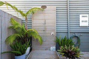 Eine Holzterrasse mit Dusche, Blumentöpfen und einem Gartenschlauch.