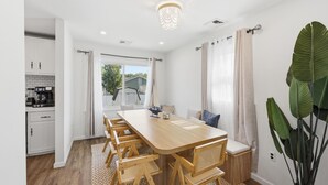 A modern kitchen with white cabinets, a wooden dining table, and a large plant. - Shore Retreat: 5 Bd home with alfresco living, hot tub, firepit, BBQ and games (Cape May)