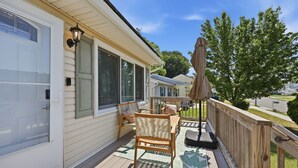 A covered deck with outdoor furniture, a sliding glass door, and a wooden fence. - Shore Retreat: 5 Bd home with alfresco living, hot tub, firepit, BBQ and games (Cape May)