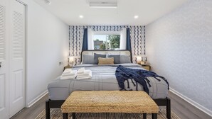 A bedroom with a bed, bedside tables, a window with curtains, a door, and a ceiling light. - Shore Retreat: 5 Bd home with alfresco living, hot tub, firepit, BBQ and games (Cape May)