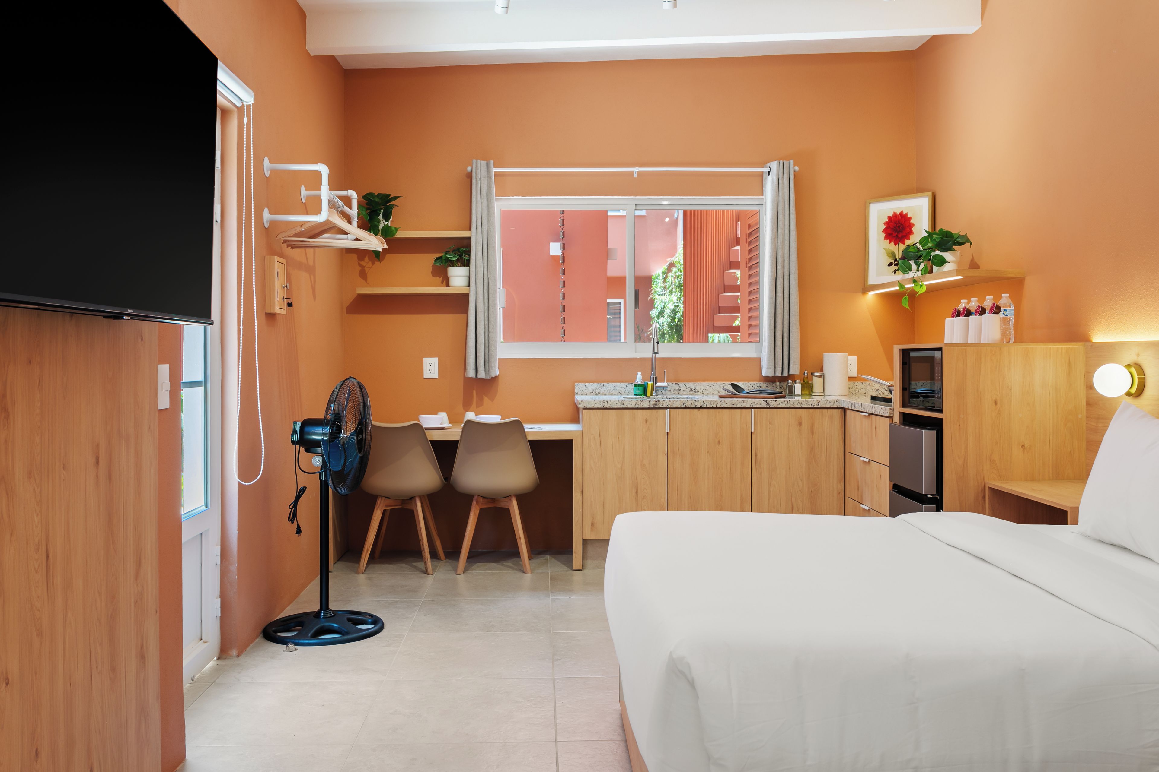 Une chambre d’hôtel de taille réduite, comprenant un lit, un bureau, une chaise, une petite kitchenette et une fenêtre.