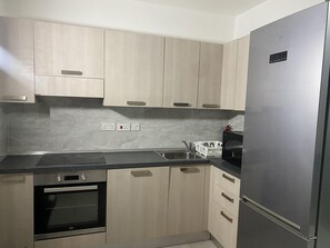 Eine Küche mit hellen Holzschränken, einem Edelstahlkühlschrank, einem Einbauofen und einer Spüle mit zwei Becken.