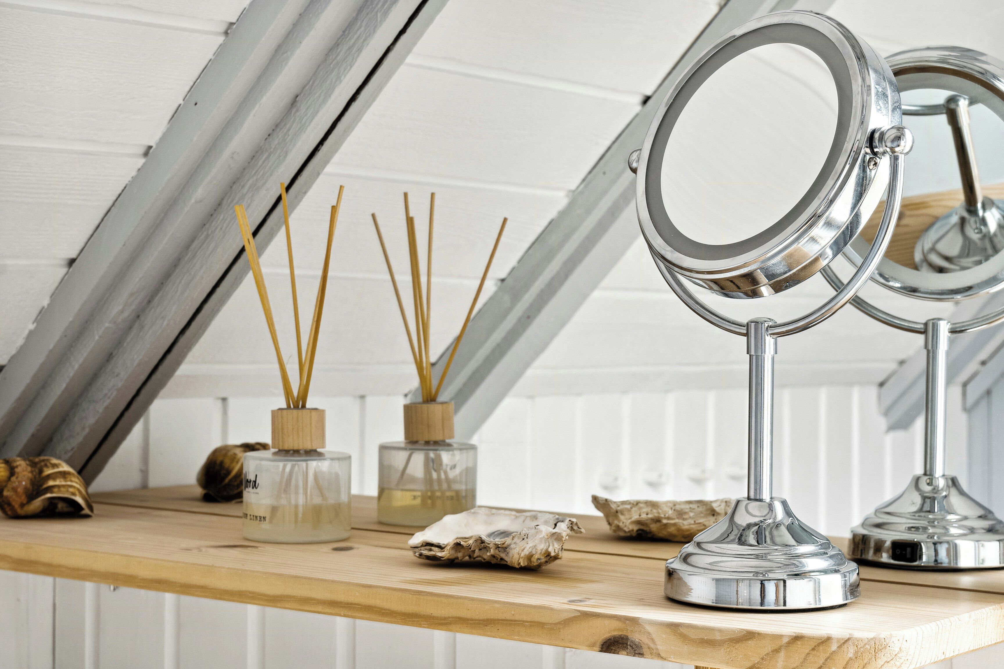 A wooden vanity with a mirror, two reed diffusers, and decorative shells.