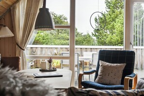 Ein gemütliches Zimmer mit großem Fenster, einem blauen Sessel, einem Tisch mit Kerze und einer Pendelleuchte.