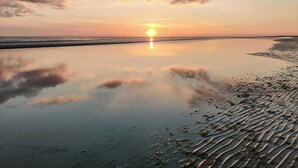 A calm beach at sunset with a clear sky and calm water reflecting the sky.
