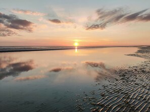 Ein ruhiger Strand bei Sonnenuntergang mit blauem Himmel und ruhigem Wasser, das den Himmel spiegelt.