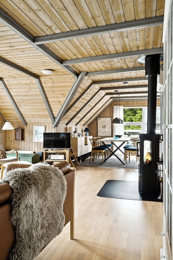 Ein gemütliches Dachzimmer mit Holzbalken, Kamin, Essbereich und Fernseher.