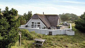 A thatched-roof house with a deck, surrounded by greenery.