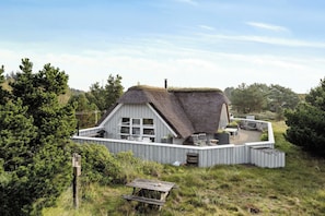 Ein Haus mit einem Reetdach und einer Terrasse, umgeben von viel Grün.