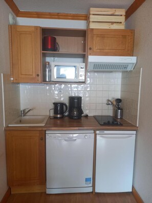 Eine kompakte Küche mit Holzausstattung, einer Mikrowelle, einer Kaffeemaschine, einem Geschirrspüler und einem kleinen Kühlschrank.