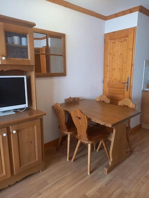 Ein Holztisch mit vier Stühlen, ein Fernseher auf einem Schrank und eine Holzt ür mit kleinem Fenster.