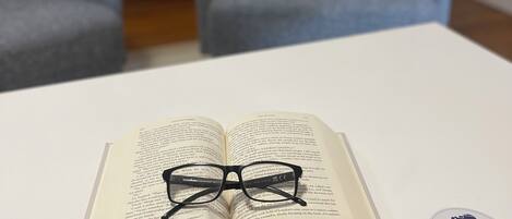 An open book with glasses on top, a white table, and a logo sticker on the table.