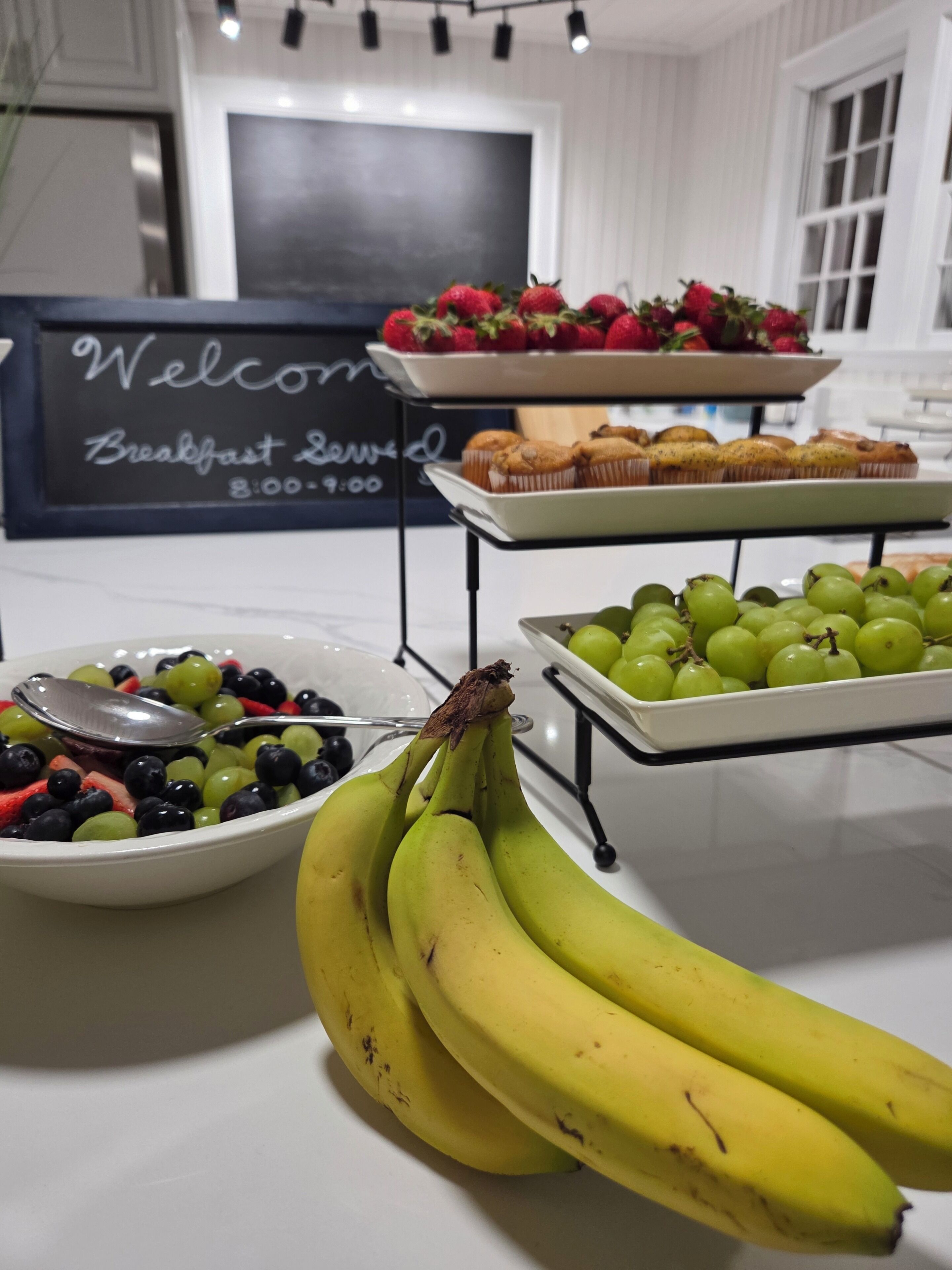 Un buffet de petit-déjeuner proposant des fruits, des muffins et un panneau indiquant les heures du petit-déjeuner.