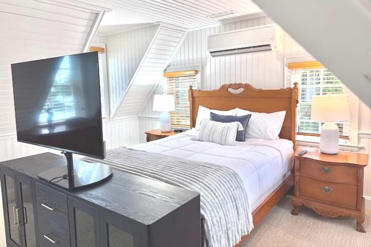 A bedroom with a bed, a TV on a cabinet, a nightstand, and a window with a view.