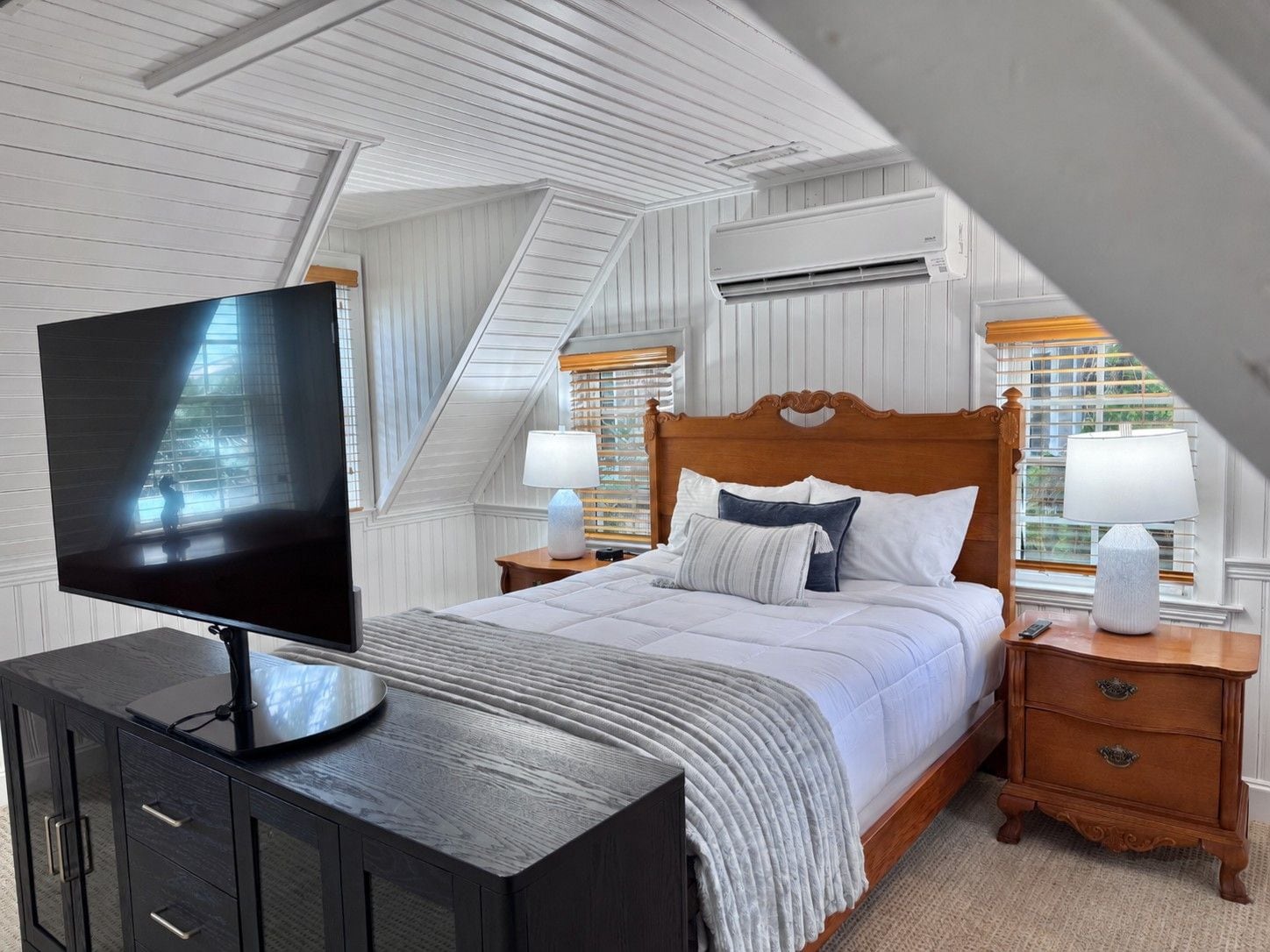 A bedroom with a bed, a TV on a cabinet, a wooden headboard, nightstands, and a window with blinds.