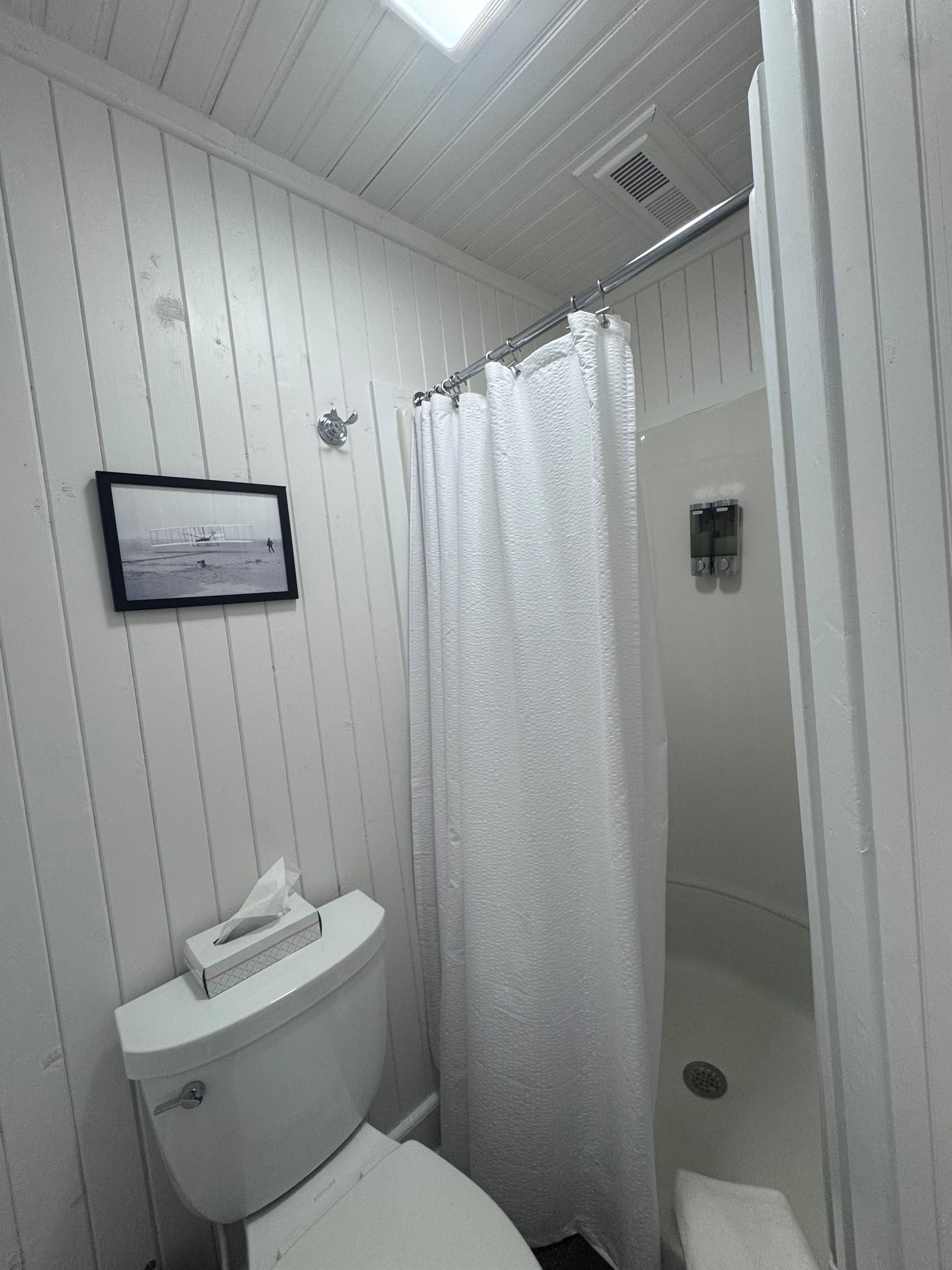 Een badkamer met een wit toilet, een douchegordijn en een inlijsting foto aan de muur.