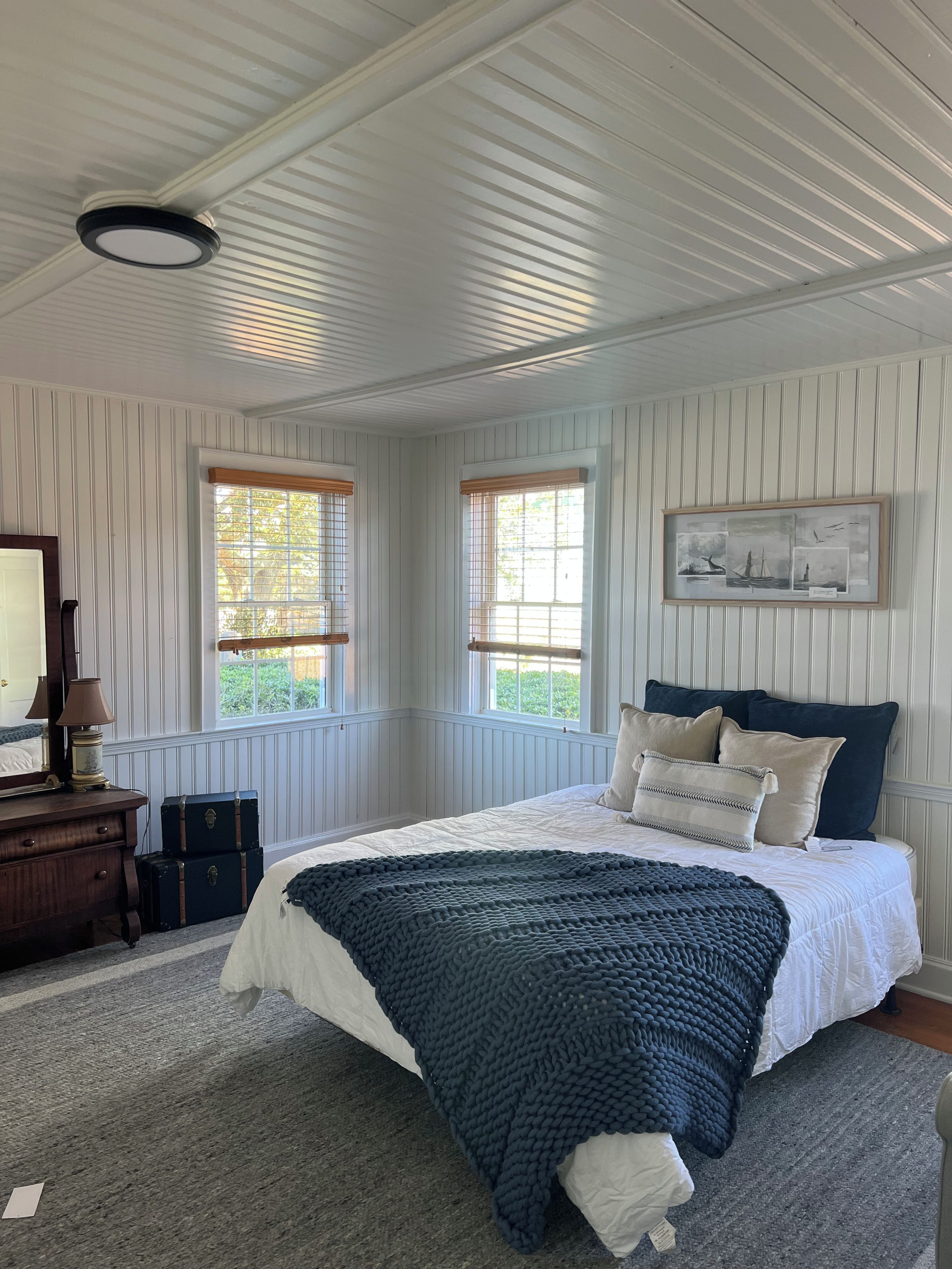 A bedroom with a bed, a dresser, a mirror, two windows, and a framed picture on the wall.