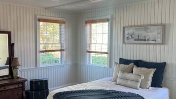 A bedroom with a bed, a dresser, a mirror, two windows, and a framed picture on the wall.