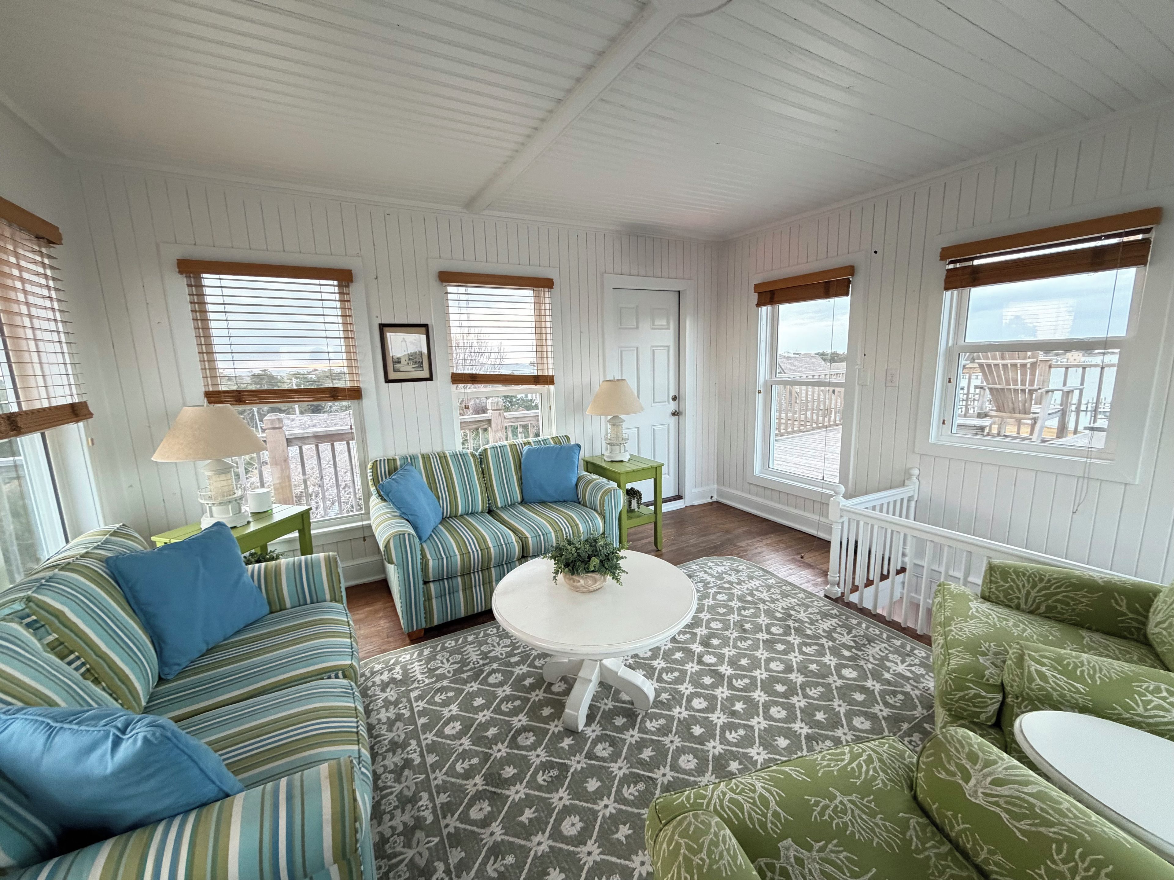 A room with a striped sofa, a green armchair, a round table, and a patterned rug.