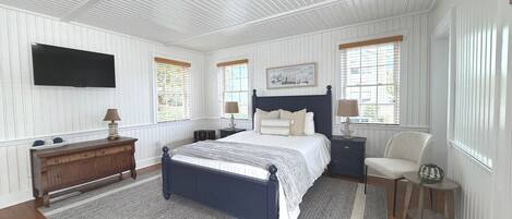 A bedroom with a bed, nightstands, a dresser, a TV, and windows with blinds.