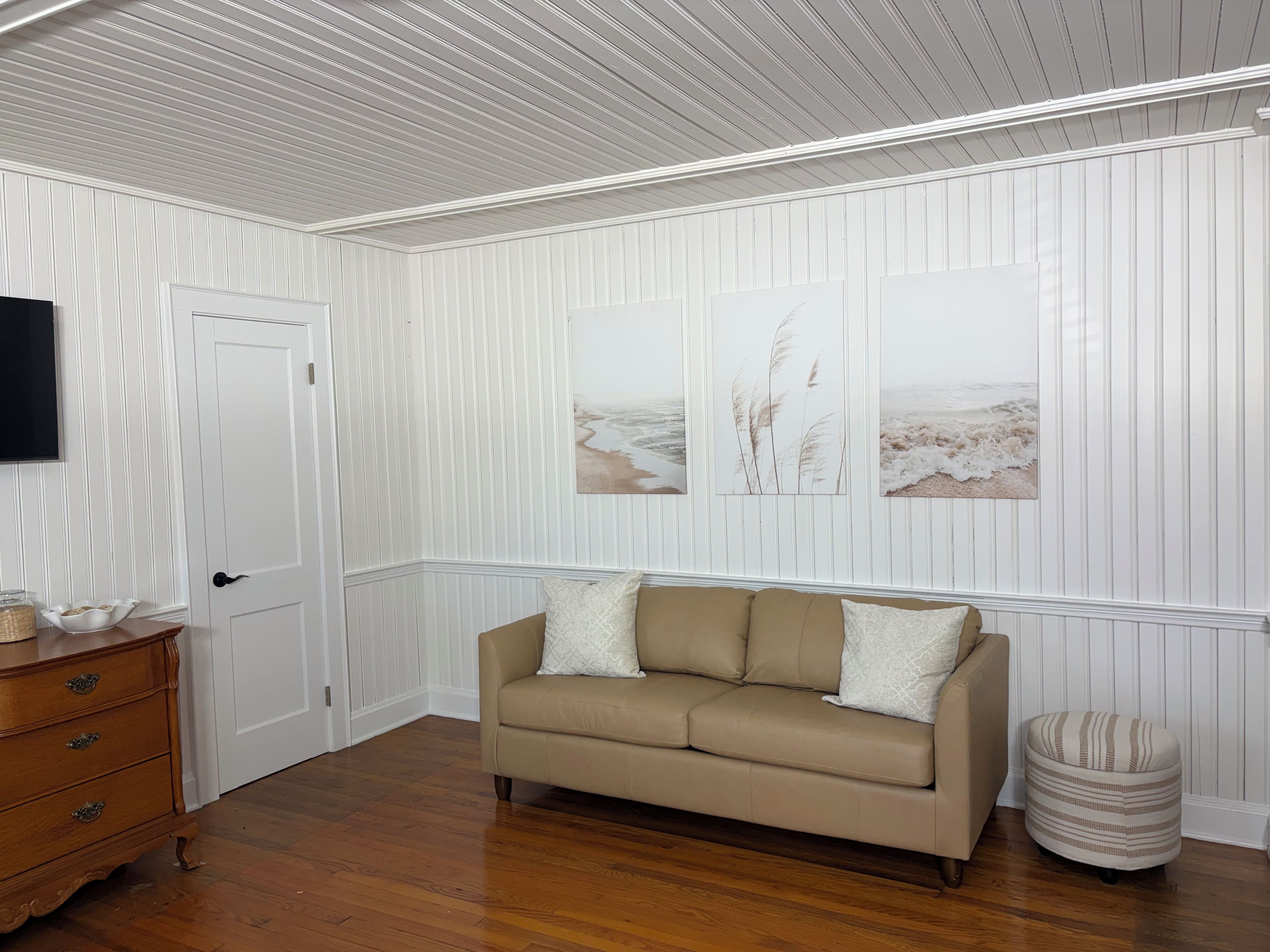 A room with a beige sofa, a wooden dresser, and a television on the wall.