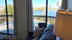 A room with a large window, a sofa, a lamp, and a view of a body of water and buildings. - Lakeside Universal Retreat (Orlando)