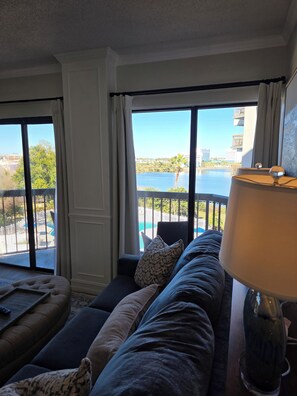 Ein Zimmer mit großem Fenster, einer Couch, einer Lampe und Blick auf ein Gewässer sowie Gebäude.