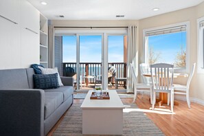 Een moderne woonkamer met een grijze bank, een witte salontafel en een balkon met buitenmeubels.