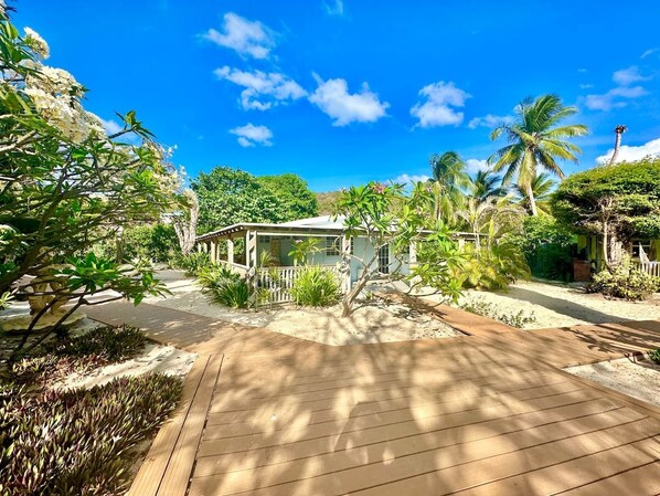 A house with a wooden deck, surrounded by tropical vegetation and palm trees. - Villa 18 Flamenco Beachfront Villas (Flamenco)