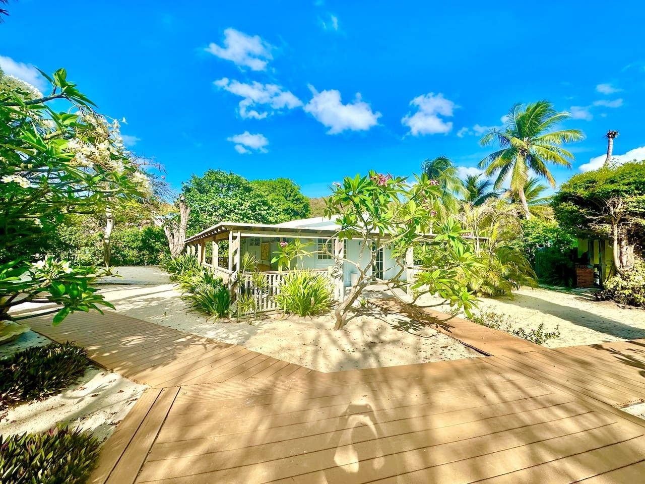 A house with a wooden deck, surrounded by tropical vegetation and palm trees.