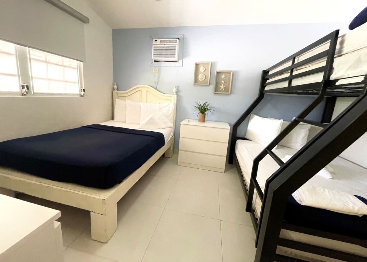 A room with a bunk bed, a single bed, a bedside table with a lamp, and a window.