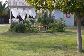 Ein gepflegter Garten mit einem Pavillon, einem Baum und einem weißen Gebäude mit einem roten, runden Objekt an der Wand.
