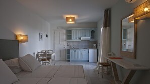 A modern hotel room with a bed, a desk, a chair, a dining table, and a kitchen area. - Double Suite 1 balcony (Naxos)