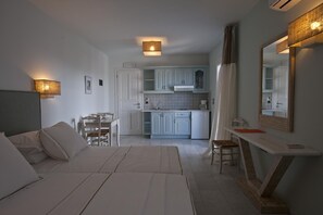 A modern hotel room with a bed, a desk, a chair, a dining table, and a kitchen area. - Double Suite 1 balcony (Naxos)