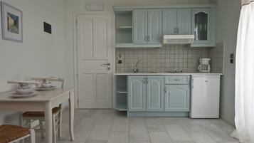 Eine Küche mit hellblauen Schränken, einem weißen Kühlschrank, einer Kaffeemaschine und einem Esstisch mit Stühlen.