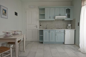 A kitchen with light blue cabinets, a white refrigerator, a coffee maker, and a dining table with chairs. - Double Suite 1 balcony (Naxos)