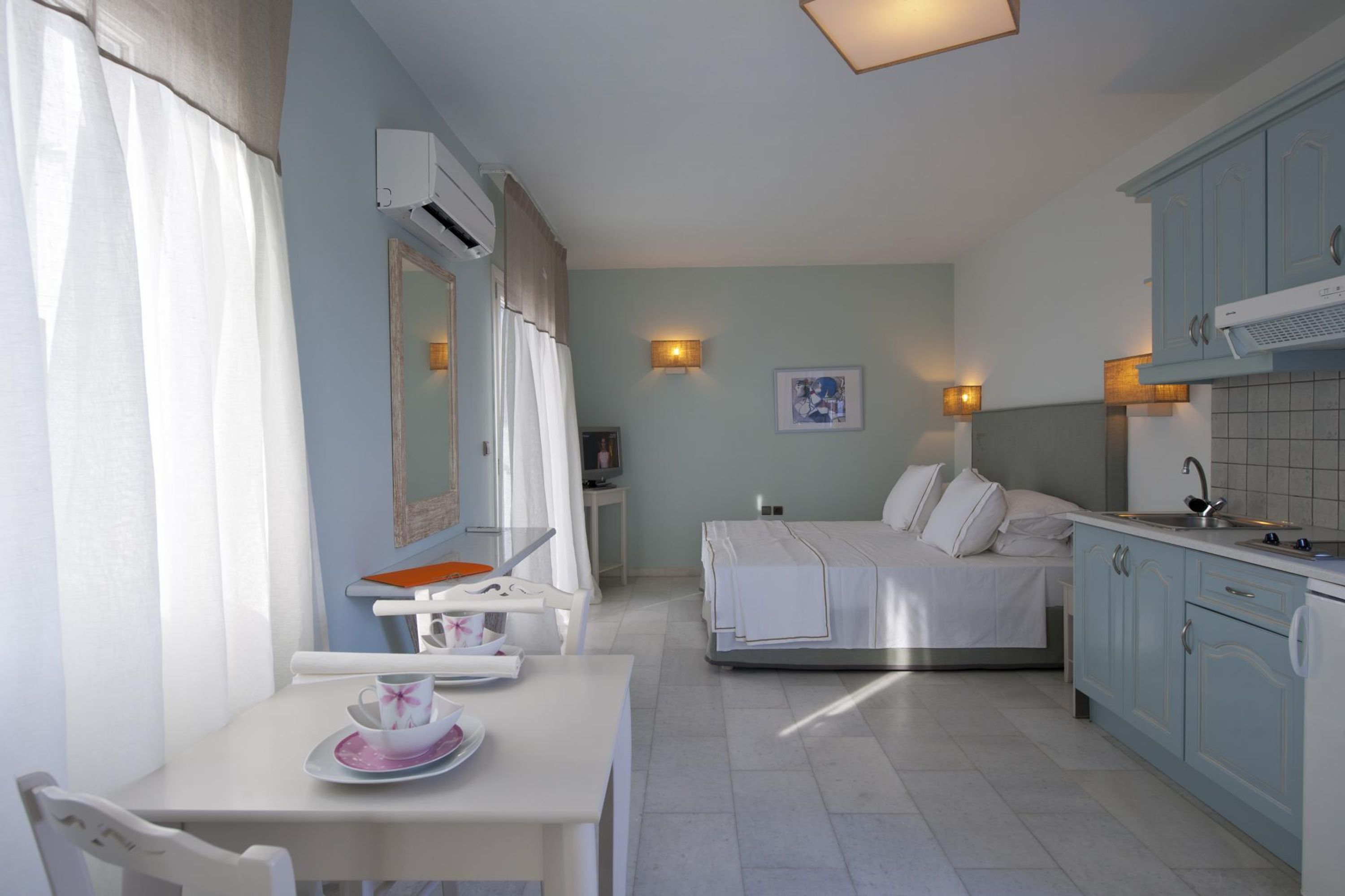 Ein kleines Hotelzimmer mit Bett, Esstisch, Küchenzeile und Bad.