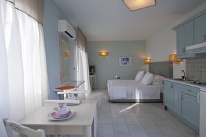 A compact hotel room with a bed, a small dining table, a kitchenette, and a bathroom. - Double Suite 2 balconies (Naxos)