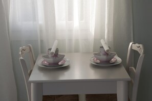 A white dining table with two white chairs, each with a pink bowl and saucer. - Double Suite 2 balconies (Naxos)