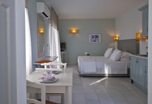 A bedroom with a bed, bedside tables, a desk with a chair, a mirror, and a wall-mounted lamp. - Double Suite 2 balconies (Naxos)