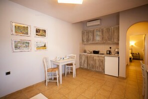 Une cuisine compacte avec un coin repas, des meubles blancs et un sol carrelé.