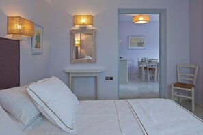 Ein Schlafzimmer mit Bett, Nachttisch, Lampe, Spiegel und Blick in einen Essbereich.