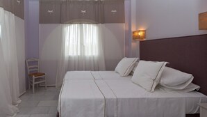 A double bed with white linens, a chair, a wall-mounted lamp, and a window with sheer curtains. - Exclusive Apartments 1st floor (Naxos)