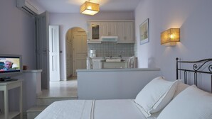 A bedroom with a bed, a TV, a small table, and a kitchenette in the background. - Exclusive Apartments 1st floor (Naxos)