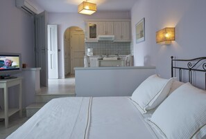 Ein Schlafzimmer mit Bett, Fernseher, kleinem Tisch und einer Küchenzeile im Hintergrund.